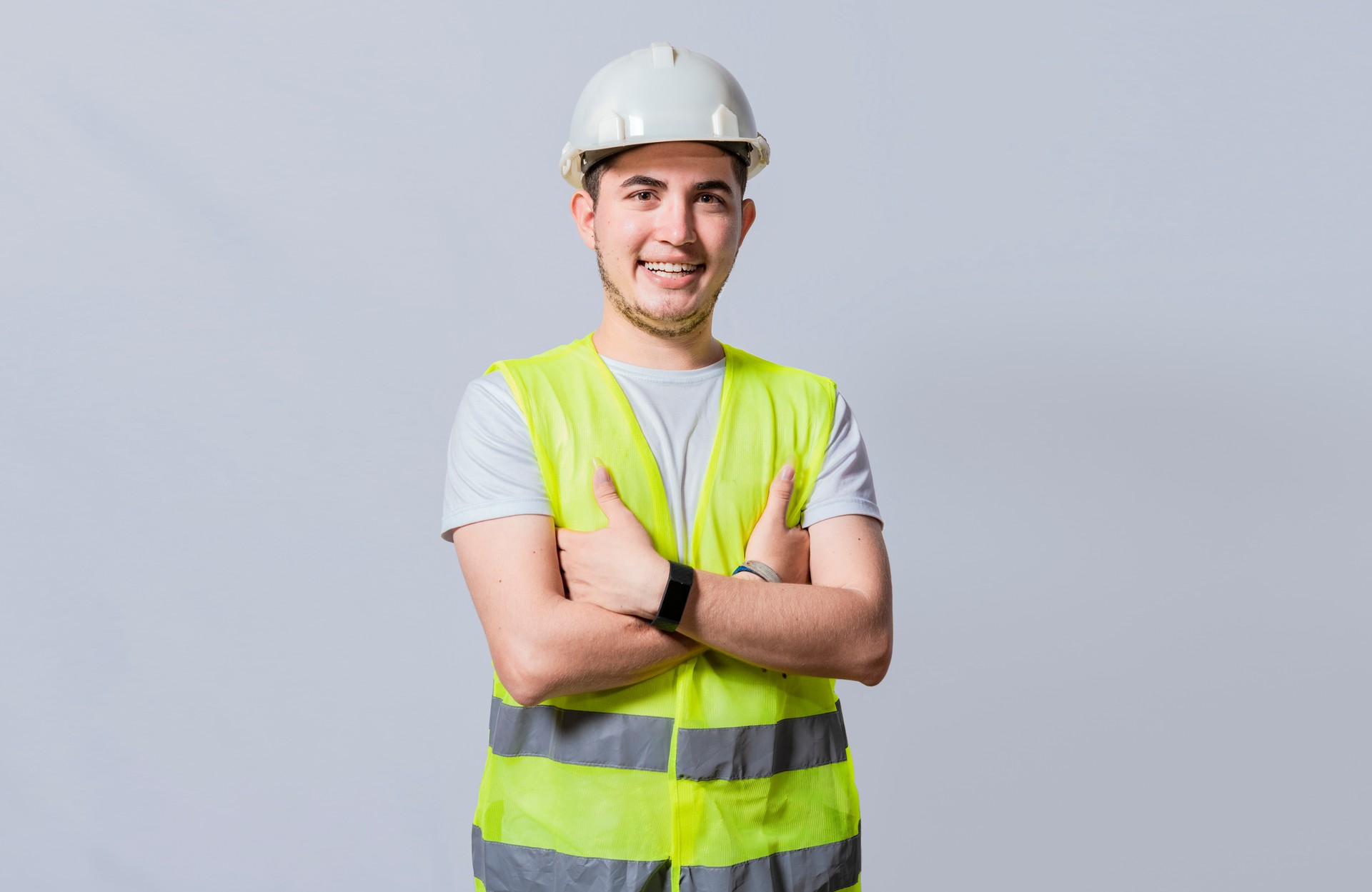 Portrait of smiling handsome engineer on white background, Portrait of young engineer wearing helmet and vest isolated. Young smiling engineer wearing helmet and vest with crossed arms isolated